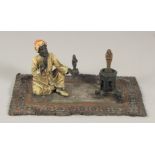 AN AUSTRIAN PAINTED COLD CAST GROUP, amulet vendor on a carpet. 7ins long.