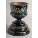 A VICTORIAN BLACK URN painted with flowers on a wooden stand. 8ins high