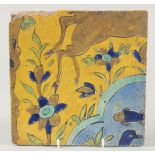 AN 18TH CENTURY PERSIAN SAFAVID YELLOW GLAZED TILE, painted with fish and flora, 23cm square.