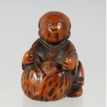 A JAPANESE CARVED WOODEN NETSUKE of a seated figure, with a fruit in his lap, with moving inset