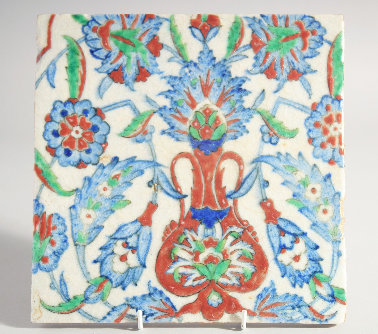 AN IZNIK STYLE GLAZED POTTERY TILE, painted with foliate motifs, 24.5cm square.