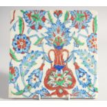 AN IZNIK STYLE GLAZED POTTERY TILE, painted with foliate motifs, 24.5cm square.