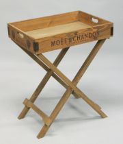 A WOODEN RECTANGULAR "CHAMPAGNE" TRAY on a folding stand. Tray 2ft 2ins long