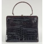 A 1940's - 1950's BLACK PATENT CROCODILE SKIN HANDBAG with fitted leather interior, brass mounts and