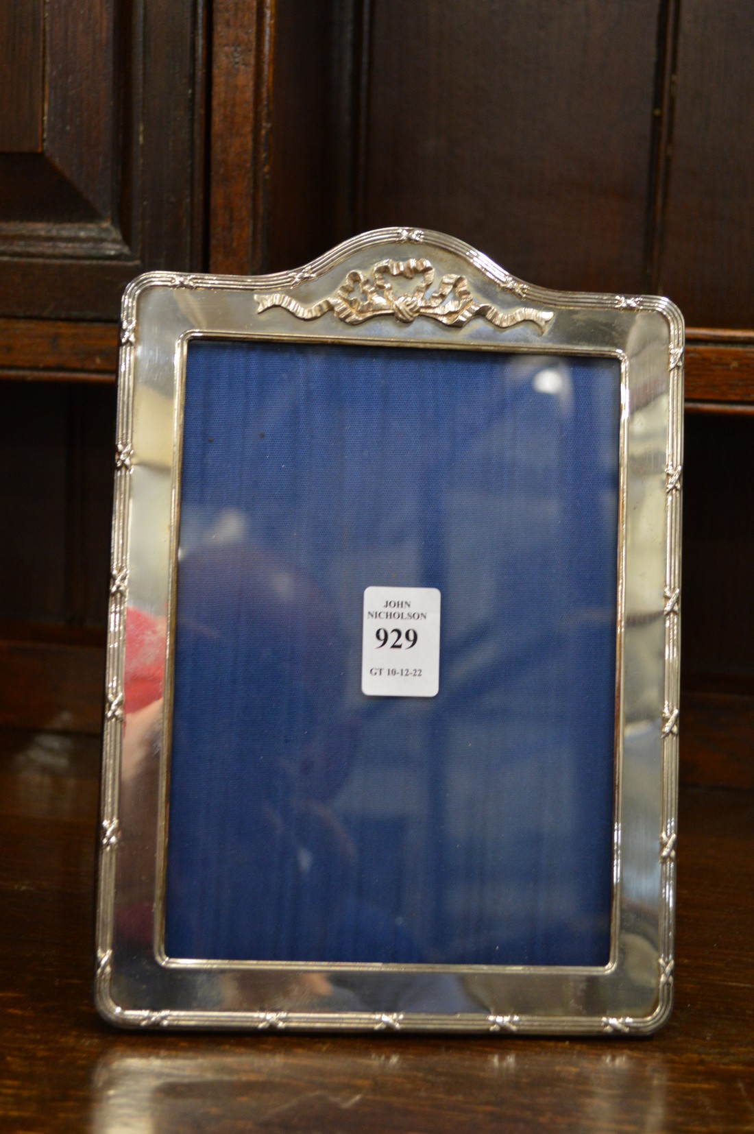 A silver photograph frame with ribbon and bow cresting.