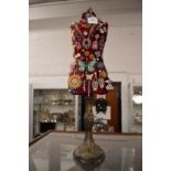 A miniature dress makers mannequin decorated with numerous brooches, pendants etc.