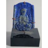 A CHINESE CARVED LAPIS LAZULI BUDDHISTIC PENDANT, on stand, the pendant measuring 5cm x 4cm.
