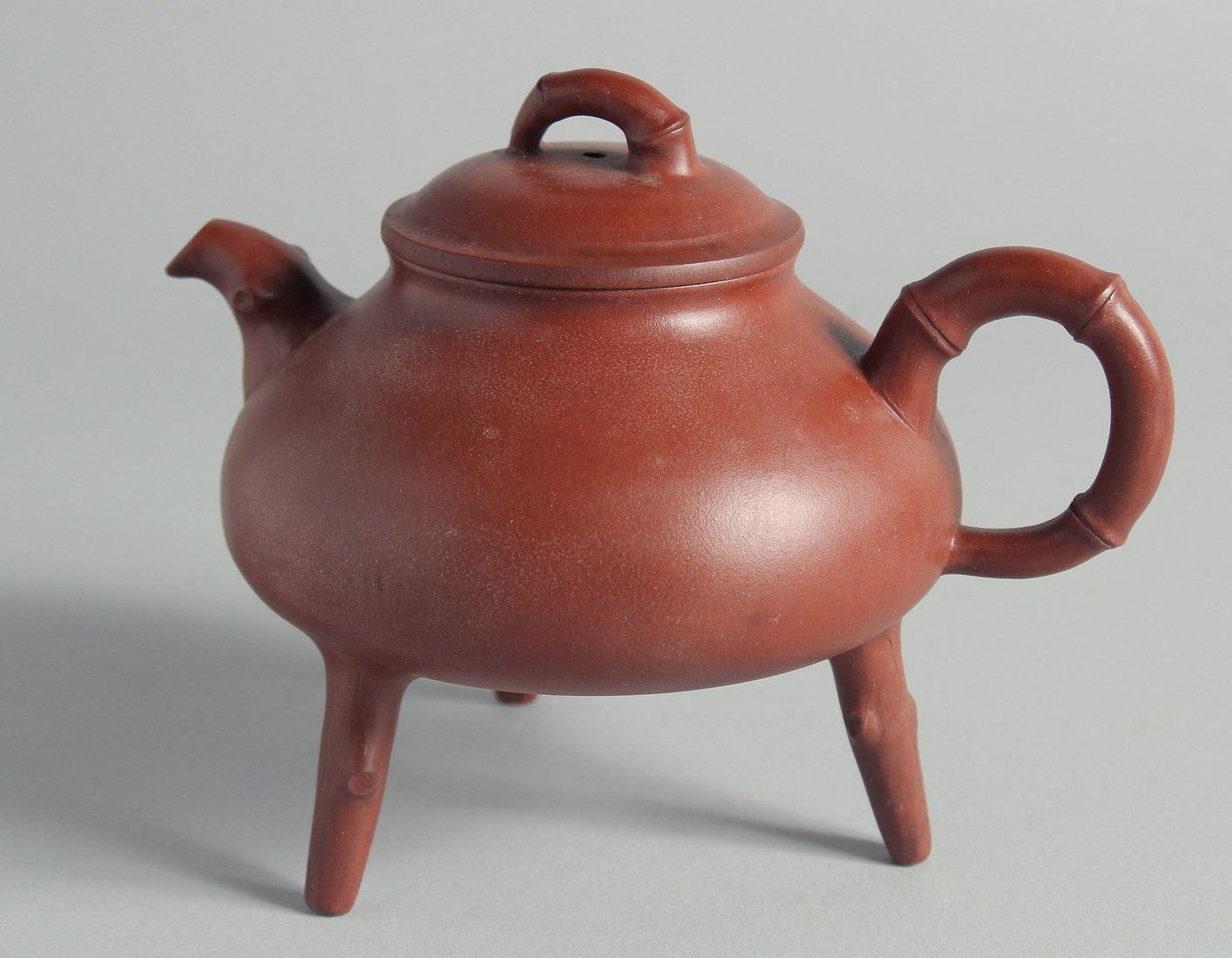 A CHINESE YIXING TEAPOT on tripod legs, with marks to inner lid and base, 13cm high.