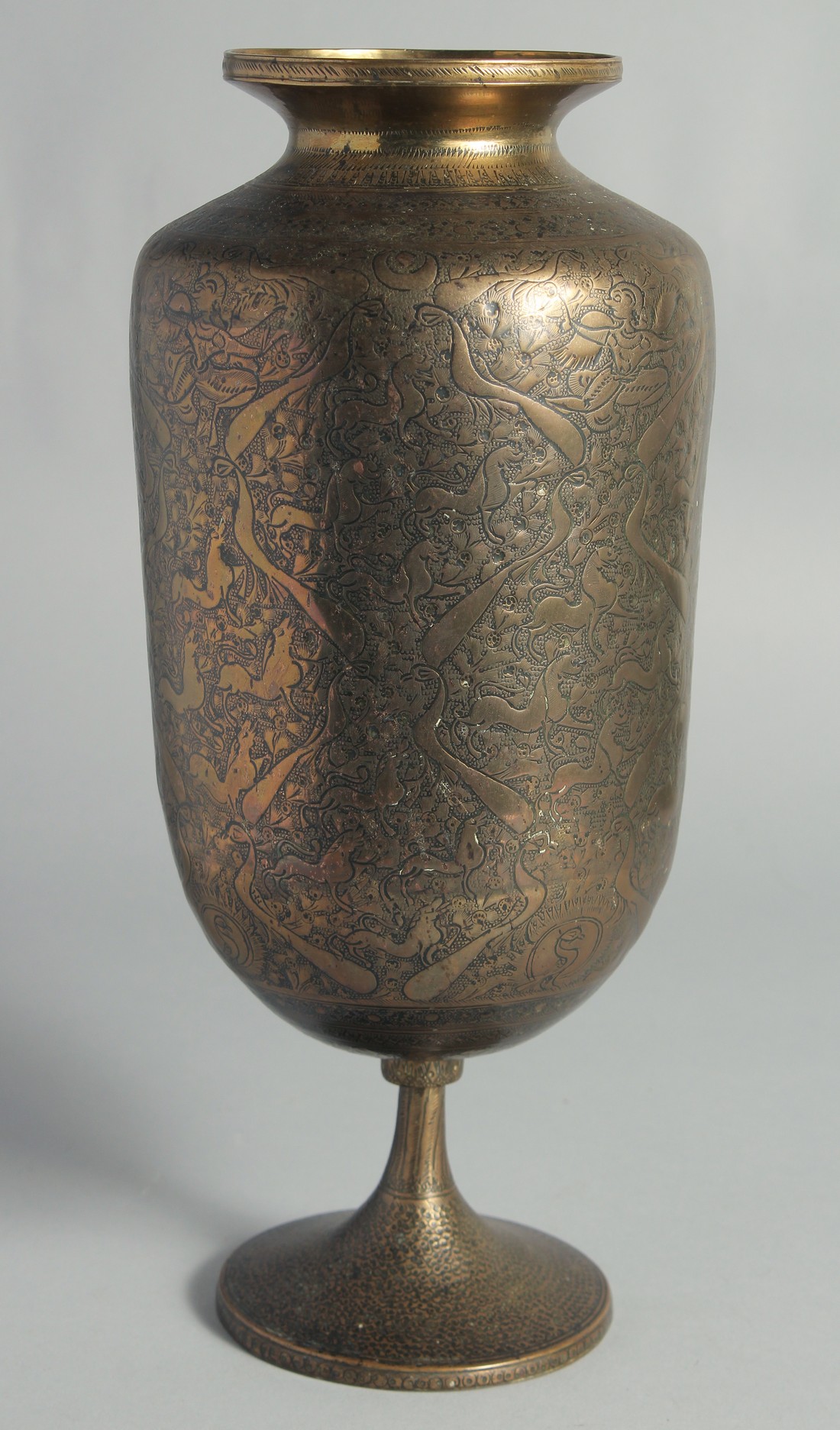 A TALL ISLAMIC ENGRAVED BRASS PEDESTAL VASE, the engraved and chased decoration depicting deities