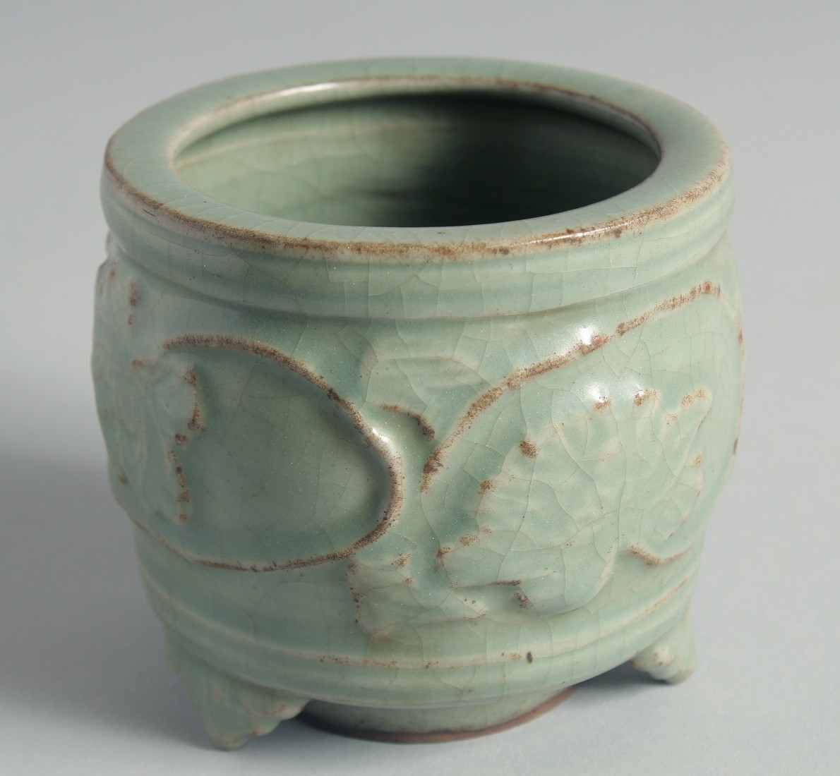 A CHINESE CELADON GLAZE CENSER, relief-decorated with leaves and vine, raised on three feet, 10cm