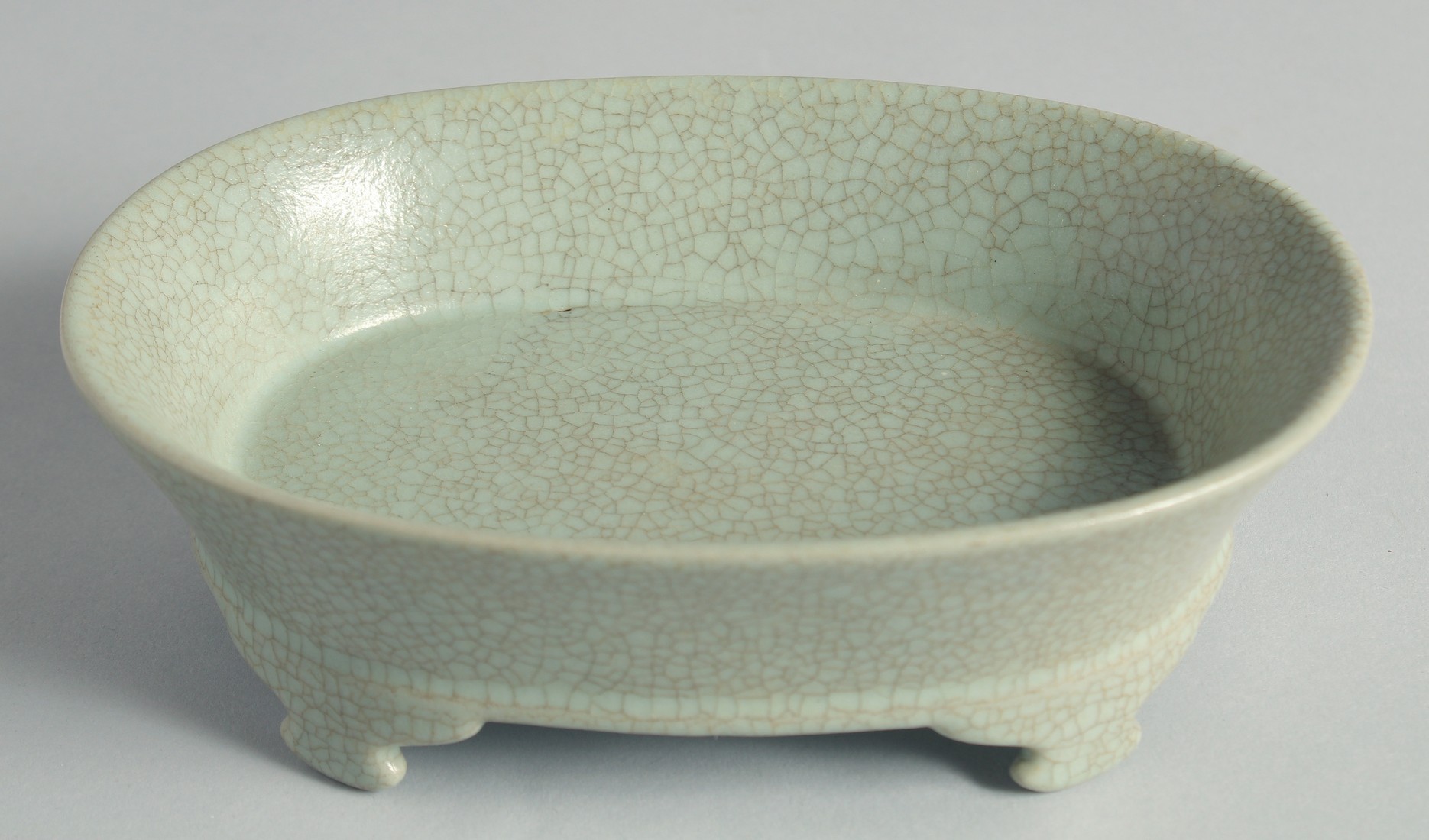 A CHINESE CELADON CRACKLE GLAZE OVAL FORM BRUSH WASHER, raised on four feet, 20cm wide.