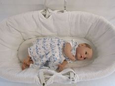 A Reborn baby doll 21" weighted doll with wide open brown eyes and painted hair with a moses basket