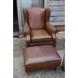 A leather wing back armchair with loose seat cushion, on turned supports, and a matching footstool