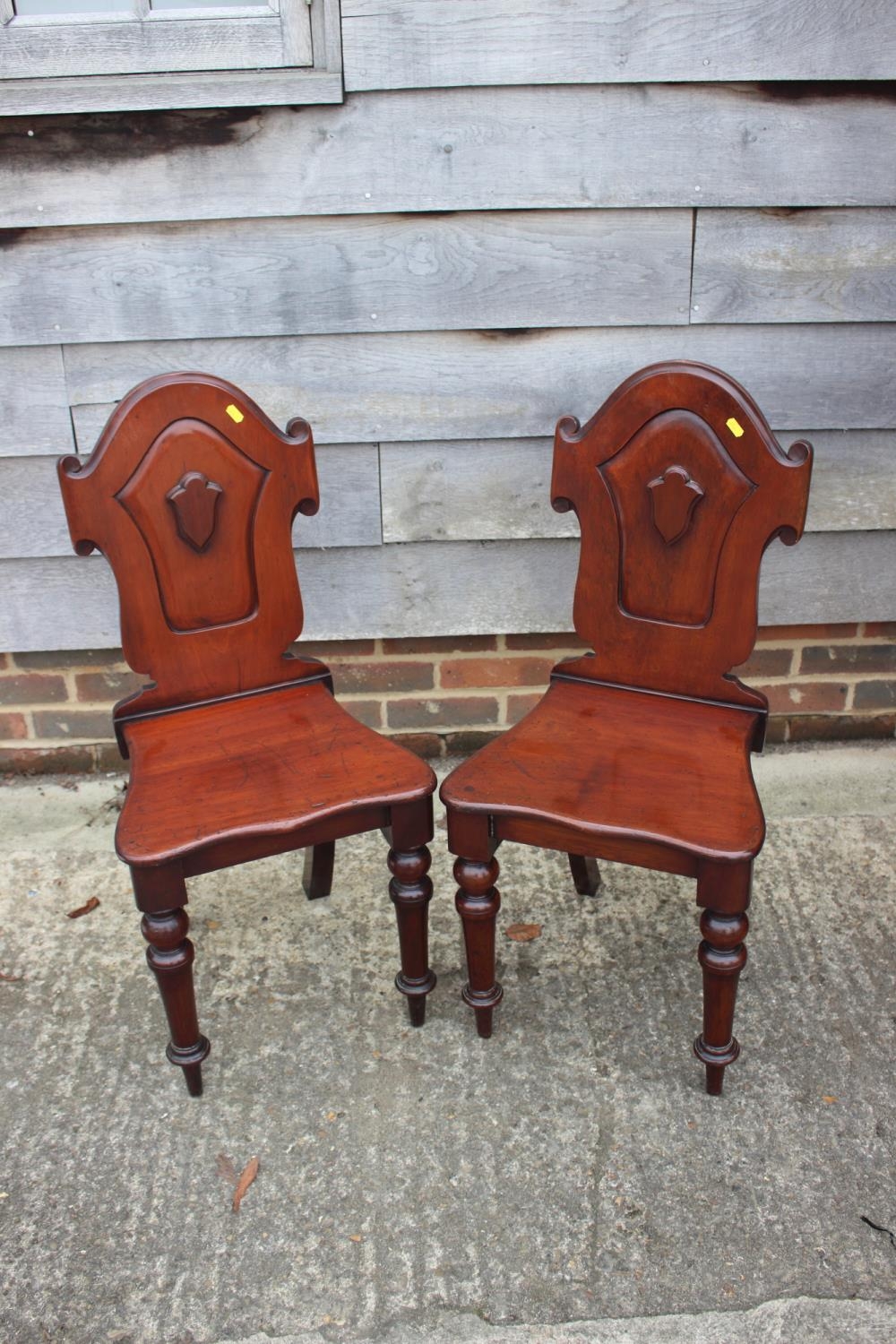 A pair of 19th century carved mahogany hall chairs with shaped panel backs, on turned supports