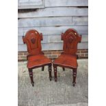 A pair of 19th century carved mahogany hall chairs with shaped panel backs, on turned supports