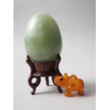 A turned jade egg, 2 1/2" high, on hardwood stand, and an amber carved elephant, 1" high