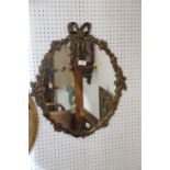 An oval gilt metal framed wall mirror with floral decoration and ribbon finial, 17 3/4" x 14 1/2",