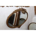 An oval gilt framed wall mirror with ribbon crest plate, 17" x 29"