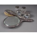 An embossed silver backed hand mirror, a silver backed brush and four silver mounted toilet jars,