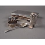 An engine turned cigarette box, two silver napkin rings, a silver teaspoon and a silver plated