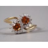An 18ct gold two stone spessartite garnet and diamond crossover ring, size M
