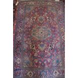 A Kerman rug with scroll and tendril design and central medallion on a plum ground in shades of red,