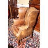 A leather wing armchair of Georgian design, on square moulded and stretchered supports