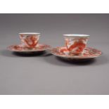 A pair of Chinese iron red and white glazed tea bowls and saucers, decorated dragons and flaming