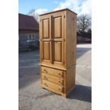A waxed pine wardrobe, the upper section enclosed two panelled doors over three drawers, on