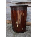 A 19th century figured mahogany and inlaid bowfront hanging corner cupboard with dentil cornice