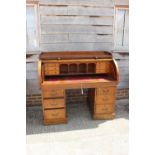 An Edwardian oak cylinder top double pedestal desk with fitted interior over six graduated