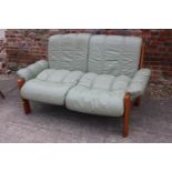 A 1970s teak frame two-seat settee, upholstered in a sage green leather with loose seat and back
