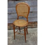 An Edwardian walnut deportment chair with caned back and seat, on stretchered splayed supports,