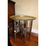 An Egyptian? circular brass topped table, on six folding turned hardwood supports, 22" dia