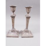 A pair of Goldsmiths and Silversmiths filled silver candlesticks of Adam design, on square bases, 9”