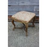 A carved giltwood stool, upholstered in a floral swag pattern fabric, on cabriole supports united by