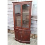 An oak serpentine fronted corner unit enclosed two glazed doors over two drawers and cupboards, on