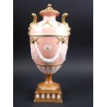 A Wedgwood urn and cover with twin gilt mask handles and relief swag decoration, on a pink ground