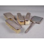 A silver backed three-piece dressing table set, comprising mirror and two brushes, and two other