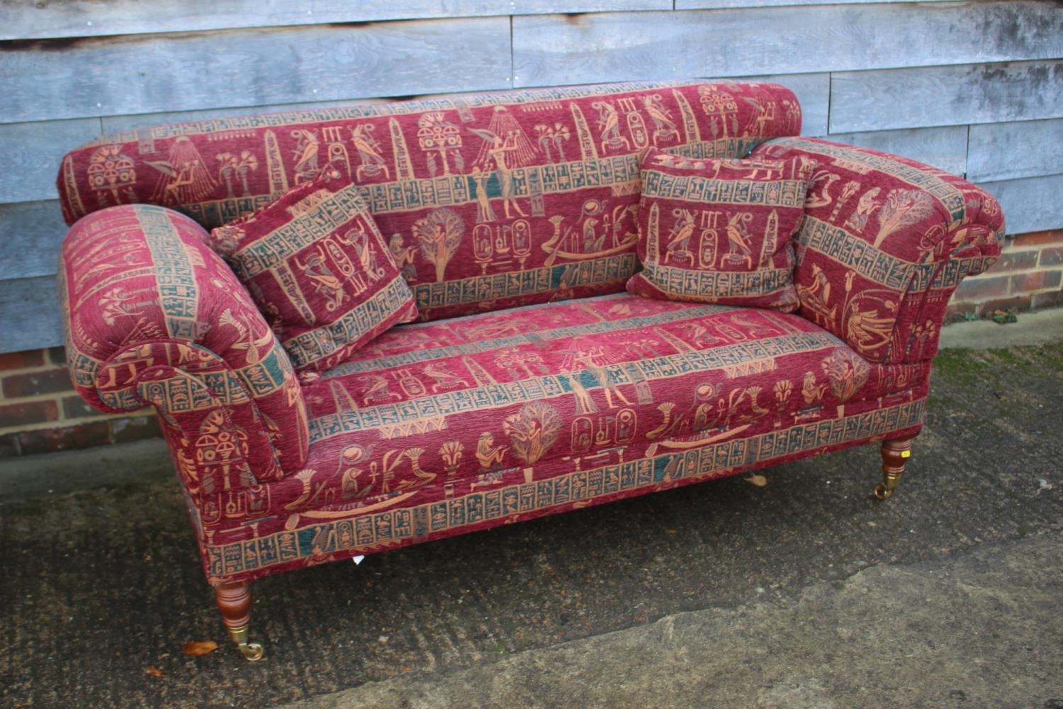 A two-seat scroll arm settee, upholstered in an Egyptian design fabric, on turned supports, 74" wide