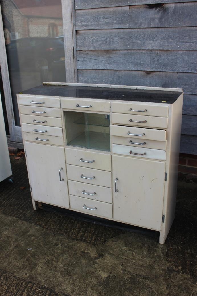 A dentist's instrument cabinet with black glass top, fitted fifteen drawers, central glazed cupboard