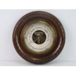 An Edwardian aneroid barometer in decorative circular wooden frame, 22cm dia, glass deficient.