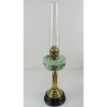 A brass oil lamp handing hand painted opaque green glass reservoir, with chimney.