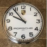 A Porsche themed dealer-type wall clock. White dial with black baton hands and Arabic numerals.