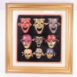 A montage of nine enamelled brass decorative masks mounted on black velvet with gold painted frame