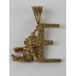 A 9ct gold pendant in the form of an 'E' with clown figure leaning upon, 2cm in length, 1.2g.