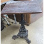 A cast iron based pub table raised over 3 outswept feet with double fish design column and wooden