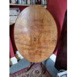 An oval tilt top half veneered walnut table raised over quatreform base, 118 x 87cm.