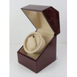 An electrically operated watch winder, glazed mahogany effect cabinet, with charger, 13cm wide.