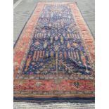 An early 20thC red and blue ground rug having geometric design of trees upon, 5 x 2.25m.